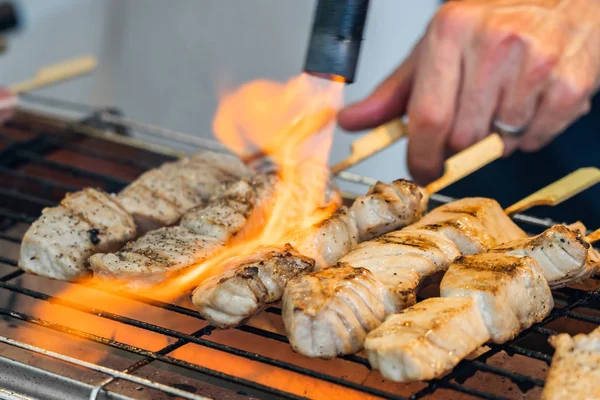 Um homem está cozinhando paus de atum fresco em uma grelha . — Fotografia de Stock