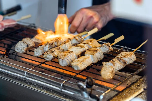 Um homem está cozinhando paus de atum fresco em uma grelha . — Fotografia de Stock