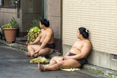 Japanese Sumo Wrestlers are Sitting and Resting on The Ground on a Street clipart