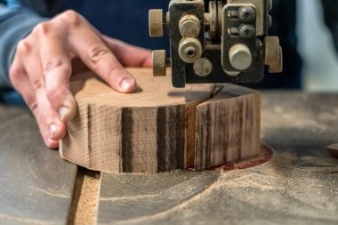 Marangoz tezgahtaki aletlerle ahşap parçayı kesiyor. Adamın eli kütükten yuvarlak bir ayrıntı çıkarıyor. Joiner atölyede kase yapmak için elektrikli testereyi kullanıyor..