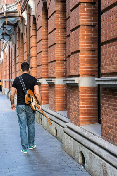 Man is Walking Away with Bass Guitar on Pedestrian Street Walkway.