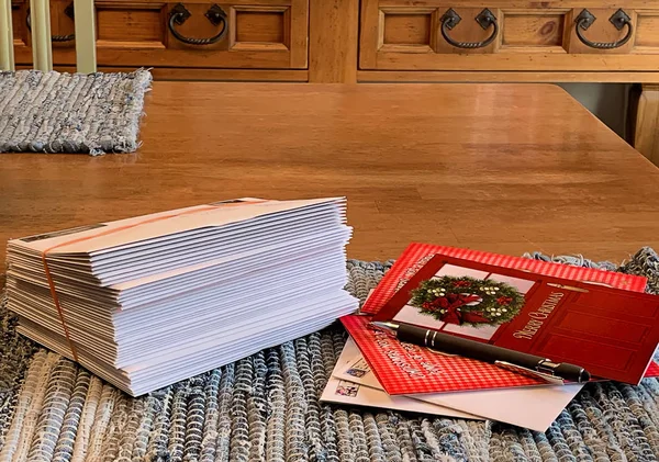 Zarflarda gönderilmek üzere hazır Noel kart yığınını. Kalem ve kartları yanlarında mutfak masasının üstünde döşeme yazma