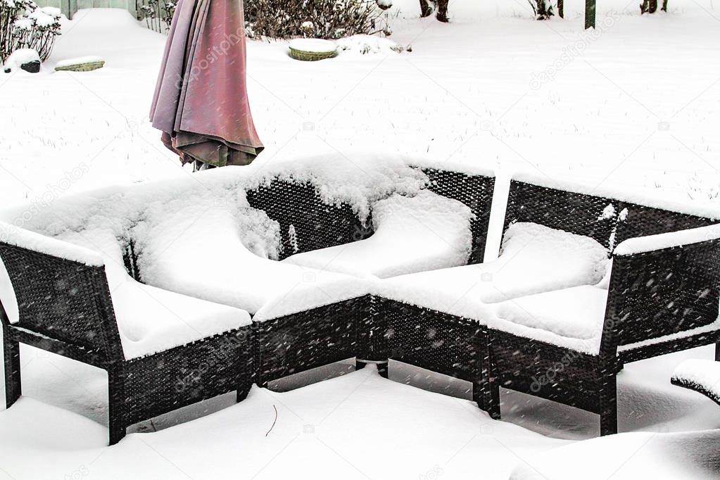 Patio furniture covered in snow after snowstorm.  Some have round table, picnic table and seating area.  Outdoors in the winter season.