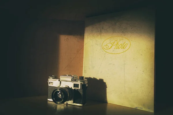 Old fashion retro analog camera standing beside big leather photo album slightly in the shadow. Old damaged photo with scratches