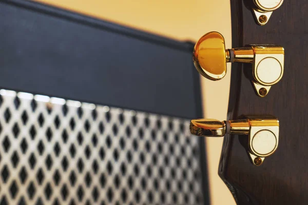 Guitar head with golden tuners in front of powerful vintage guitar amplifier with shiny metal grill