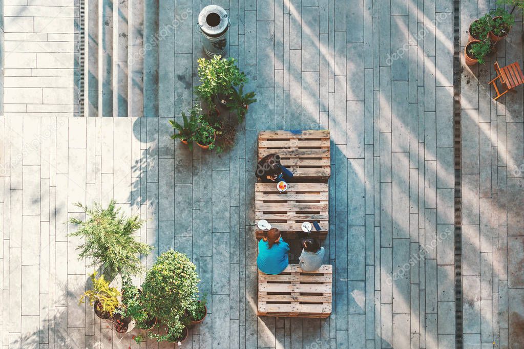 People hanging out in the garden, sitting on the pallets eating cakes. View from above. Concept