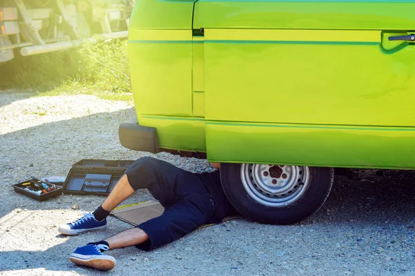 Eski altında yatan genç erkek hipster Zamanlayıcı camper van yol kenarında onarmaya çalışmak