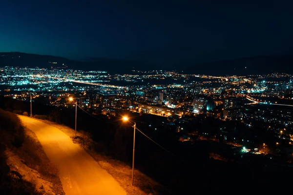 Wgląd nocy z ponad stolicy Gruzji, Tbilisi. Oświetlenie uliczne i wzgórzach otaczających miasto. Błękitne niebo. -Obraz — Zdjęcie stockowe