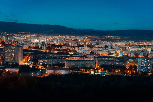 Luftaufnahme, nächtliche Stadtansicht mit Nachthimmel. natürliche freie Sicht über große Stadtblöcke mit Straßenlaternen und Hügeln drumherum - Bild — Stockfoto