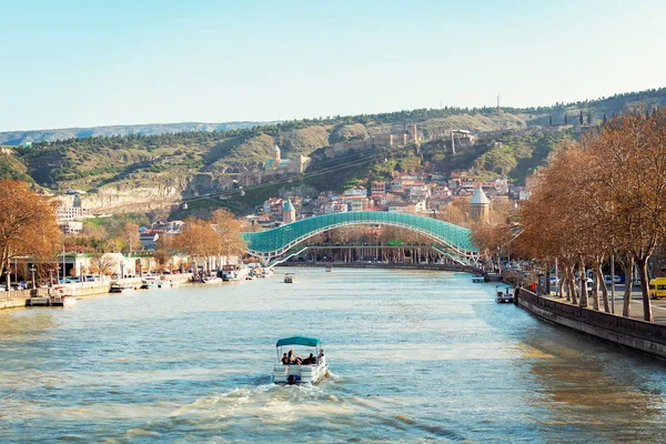 Осінь в Тбілісі, Грузія. Панорамний вид над знаменитим скляним мостом миру і старим містом під давньою фортецею. Човен пливе по річці.. — стокове фото