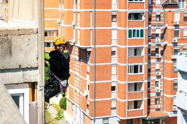 İp erişimi ve yükseklik inşaatı projesiyle uğraşan erkek işçi. Duvar yalıtımı ve ön cephe boyama işi üzerinde çalışıyorum. Zorlu ve tehlikeli çalışma ortamı