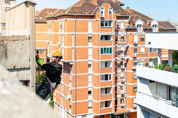 Male worker hanging on rope access and height construction project. Working on building wall insulation and facade painting decoration job. Tough and dangerous working environment