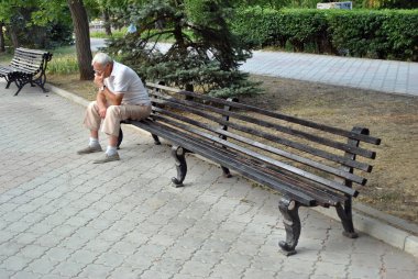 Yaşlı adam parkta bankta oturuyor.