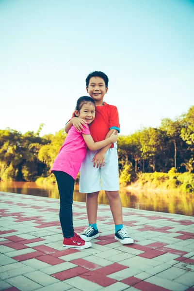 スポーツウェアの笑顔とハグでアジアの子供 親切兄妹 夏の日の太陽の光と屋外の世話します 愛すると兄弟概念の接合します ビンテージ フィルム フィルター効果 — ストック写真