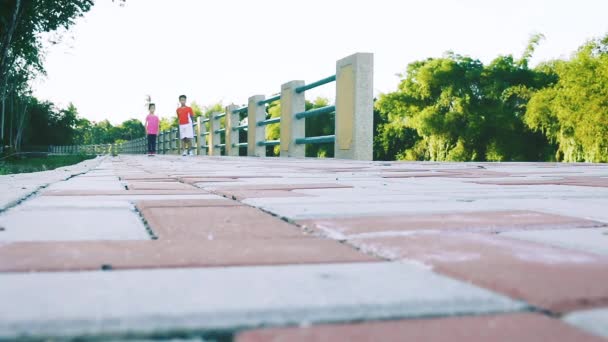 実行している アジア子供スポーツウェア公共の公園でジョギング ランナー 屋外の夏の日に明るい日光の下で 彼の妹を世話親切の弟 健康的なライフ スタイル — ストック動画