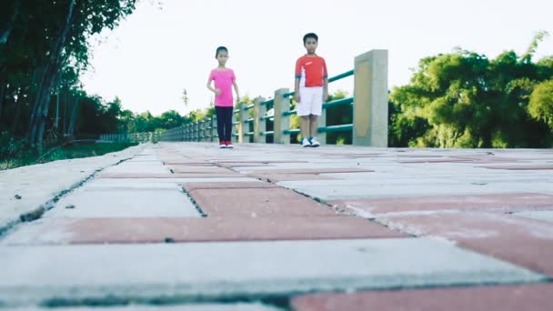 実行している アジア子供スポーツウェア公共の公園でジョギング ランナー 屋外の夏の日に明るい日光の下で 彼の妹を世話親切の弟 健康的なライフ スタイル — ストック動画