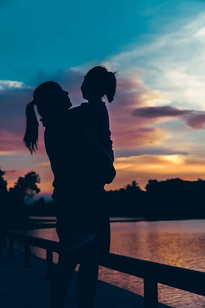 Silhouette of mother carrying her daughter and enjoying view in the morning, cozy mood. Colorful pastel sky sunrise, serenity background. Happy family spending time together. Travel on vacation.