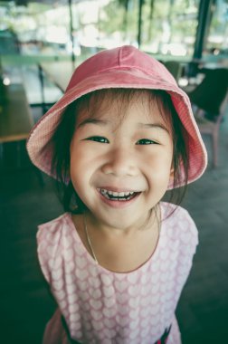 Kafede mükemmel gülümseme ile gülümseyen güzel Asyalı çocuk. Mutlu kız kamera, o kalp şekli desen ve şapka pembe elbise bakarak. Vintage film filtre efekti.