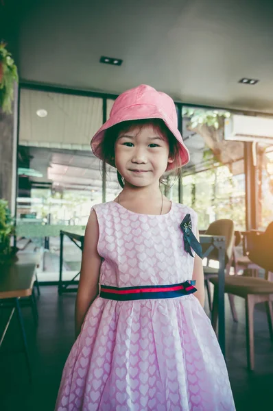 可爱的亚洲孩子微笑着 在咖啡馆完美的微笑 快乐的女孩看着相机 她穿着粉红色的礼服与心形图案和帽子 老式胶片过滤效果 — 图库照片