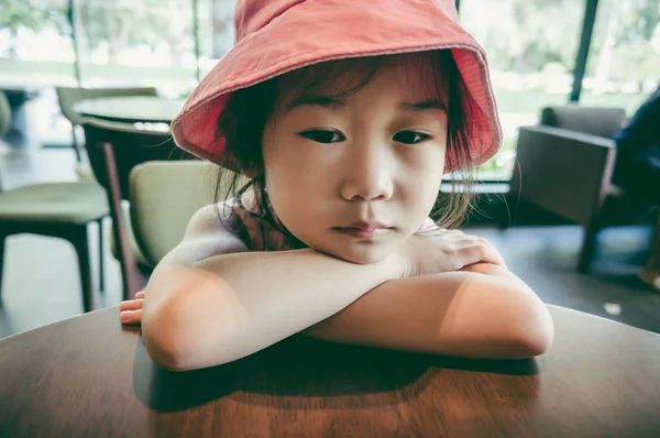 クローズ アップ ピンク帽子悲しい気持ちやよそ見 退屈で コーヒー ショップで子供の感情との不幸なアジアの女の子 ビンテージ フィルム フィルター効果 — ストック写真