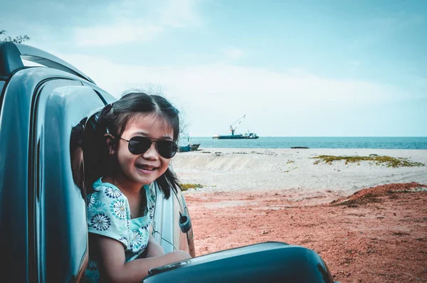 Happy asian girl in sunglasses smiling with perfect smile at beach while sitting in car. Outdoor on summer day. Travel on vacation concept. Teal and orange filter
