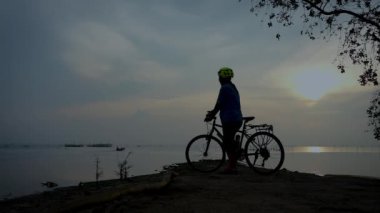 Ayakta ve balıkçı tekneleri uzaklara yelken seyir bisikletçi kadın silüeti. Deniz gündoğumu sabah, rahat ruh hali üzerinde güzel doğada sağlıklı aktif yaşam tarzı zevk Bisiklet kadınla. 