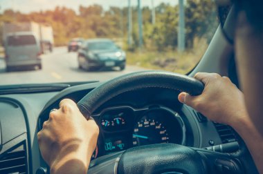 Direksiyon simidi sıkı tutan insan el. O orman yolda sürüş araba. Açık havada yaz gününde parlak güneş ışığı ile. Vintage film filtre efekti.