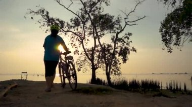 Egzersiz germe, sahil, Bisiklet ile yürüyen bisikletçi kadın silüeti. Kadın motorcu deniz gündoğumu sabah, rahat ruh hali üzerinde güzel doğada sağlıklı aktif yaşam tarzı zevk.