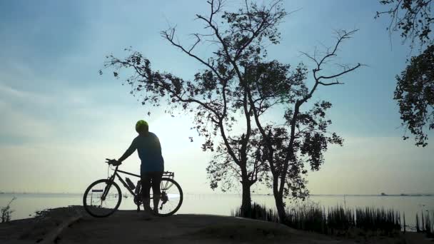 骑自行车的妇女在海边散步的剪影 伸展运动 女性车手在美丽的大自然中享受健康活跃的生活方式早晨的日出 舒适的心情 — 图库视频影像