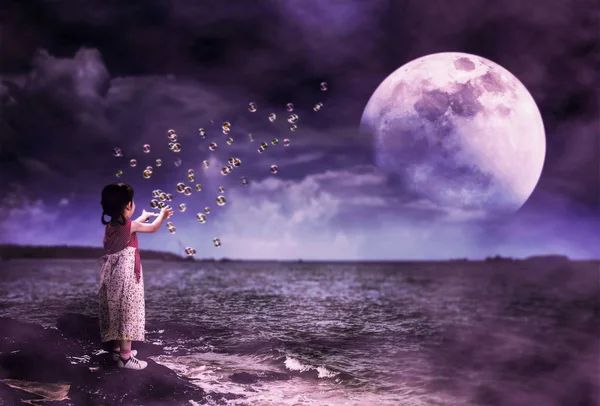 在海边的石头上玩肥皂泡的亚洲女孩的背面视图 夜空的景观与超级月亮背后的部分云 美丽的宁静背景 用我自己的相机拍摄的月亮 — 图库照片