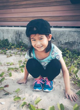 Asyalı çocuk üzerinde kum kazma eğlenceli mutlu. Gülümseyen ve plaj kameraya bakarak çekici genç kız. Yaz gününde parlak güneş ışığı ile açık. Çocuklar hakkında kavram doğada mutlu.