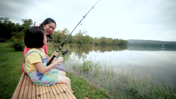 亚裔母亲在钓鱼时与女儿交谈 这对夫妇坐在一个宁静的傍晚泻湖岸边 女孩正愉快地拿着一根钓鱼竿 — 图库视频影像