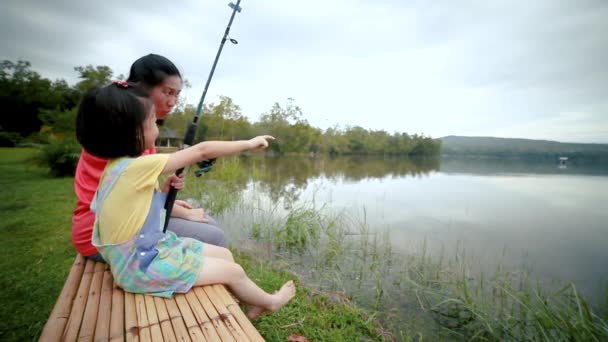 アジアの母親は 釣りをしながら 彼女の娘に話し カップルは静かな夜のラグーンのほとりに座っています 女の子は幸せに釣り竿を持っている — ストック動画
