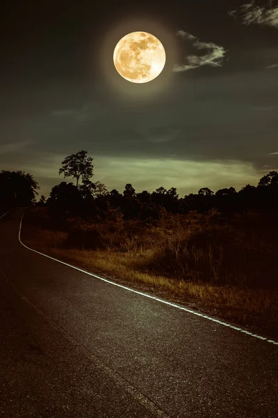 Dark sky with full moon and roadway through suburban zone.