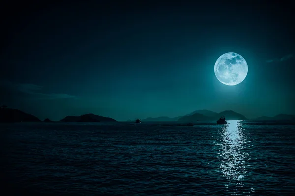 Vista panorámica del pequeño barco en aguas tranquilas del mar por la noche y la luna llena . — Foto de Stock