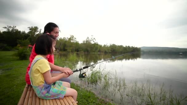 竹のごみの側に彼女の娘側とアジアの母親 湖の風景に対して釣りながら 幸せな女の子は彼女の手の中にロッドを引く 自然と子どもをつなぐというコンセプト 休暇中の旅行 — ストック動画