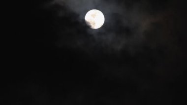 Karanlık gökyüzünde parlayan güzel dolunay. Hızlı hareket eden siyah bulutlar gerçek zamanlı olarak ayın üzerinden geçiyor. Ay bulutlar tarafından gizlendi. Gece vakti dışarıda..