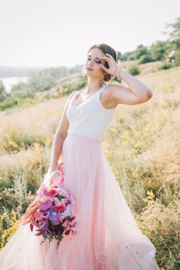 Şatafatlı beyaz ve pembe gelinlikli gelin gün batımında doğada