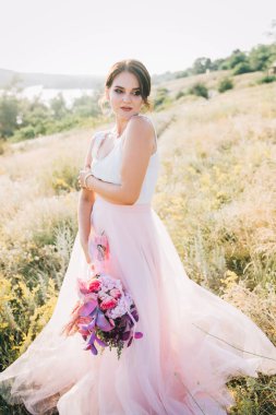 Şatafatlı beyaz ve pembe gelinlikli gelin gün batımında doğada