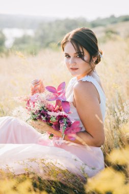 Şatafatlı beyaz ve pembe gelinlikli gelin gün batımında doğada