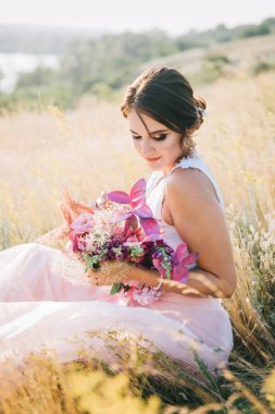 Şatafatlı beyaz ve pembe gelinlikli gelin gün batımında doğada