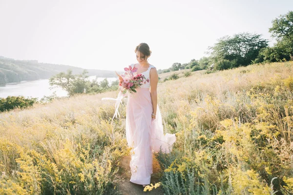 Şatafatlı beyaz ve pembe gelinlikli gelin gün batımında doğada