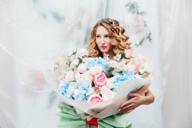 Yüzünde güzel makyajı ve saç stili olan güzel bir kız büyük bir buket çiçekle kozmetik bilimci ve çiçekçi reklamı yapıyor.