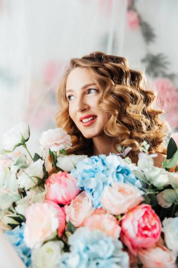 Yüzünde güzel makyajı ve saç stili olan güzel bir kız büyük bir buket çiçekle kozmetik bilimci ve çiçekçi reklamı yapıyor.