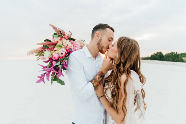 Love Story of a beautiful couple in a pink wedding luxury dress with a bouquet in the Sahara desert, sand, dunes