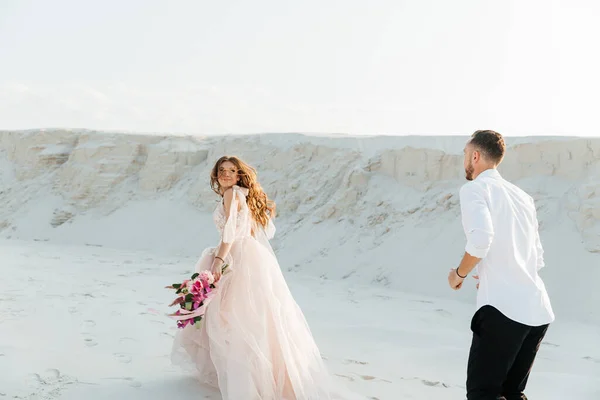 Güzel bir çiftin aşk hikayesi. Pembe bir gelinlik içinde Sahra Çölü 'nde bir buketi olan kumlar ve kumullar.