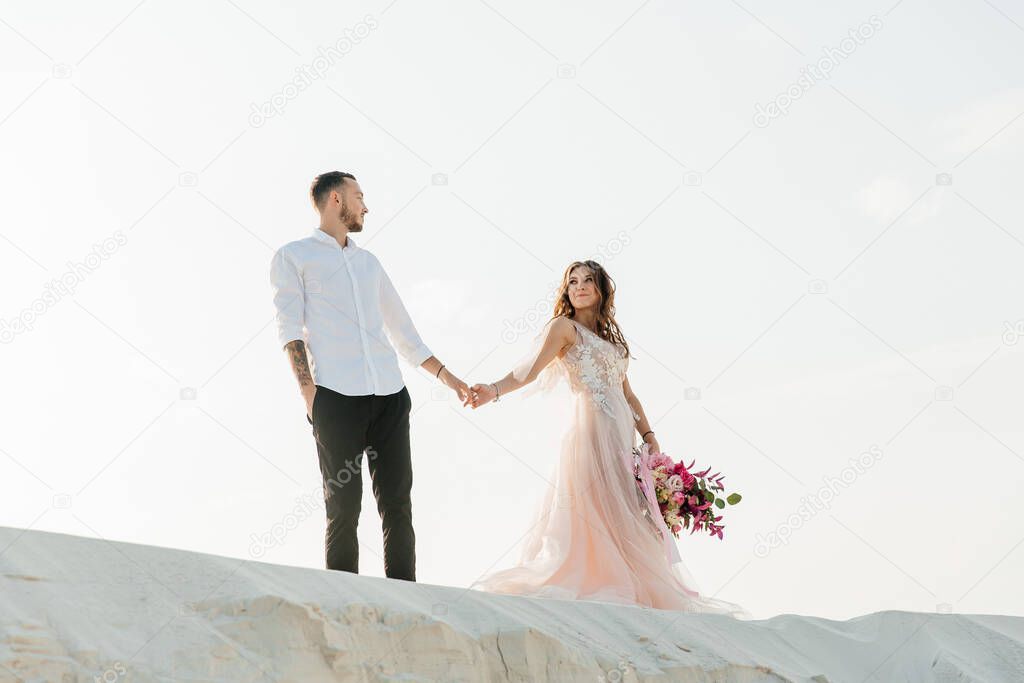 Love Story of a beautiful couple in a pink wedding luxury dress with a bouquet in the Sahara desert, sand, dunes