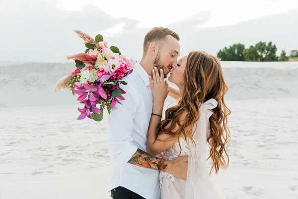 Love Story of a beautiful couple in a pink wedding luxury dress with a bouquet in the Sahara desert, sand, dunes