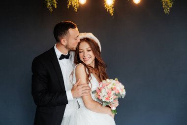 Damadın siyah takım elbiseli ilk buluşması ve beyaz gelinlikli gelinin beyaz ve siyah arka planda bir fotoğraf stüdyosunun içinde bir buket olması.