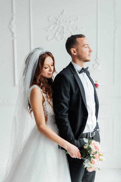 The first meeting of the groom in a black suit and the bride in a white wedding dress with a bouquet in the interior of a photo studio on a white and black background